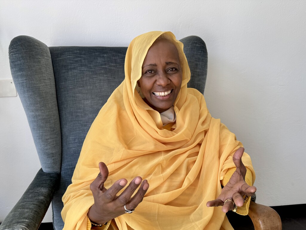 Die Sudanesin Rabab Baldo sitzt in einem Sessel, lächelt und gestikuliert