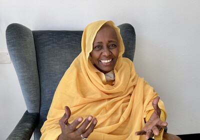 Die Sudanesin Rabab Baldo sitzt in einem Sessel, lächelt und gestikuliert