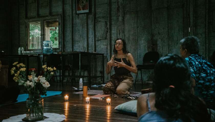 A woman sits on the floor, candles burning in front of her. She leads a ritual with the workshop participants