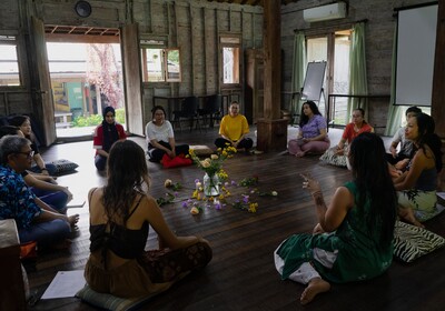 Eine Gruppe Workshopteilnehmer:innen sitzt im Kreis am Boden um eine Vase mit Blumen.
