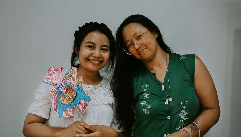 Two workshop participants smile into the camera, one shows their shadow puppet.