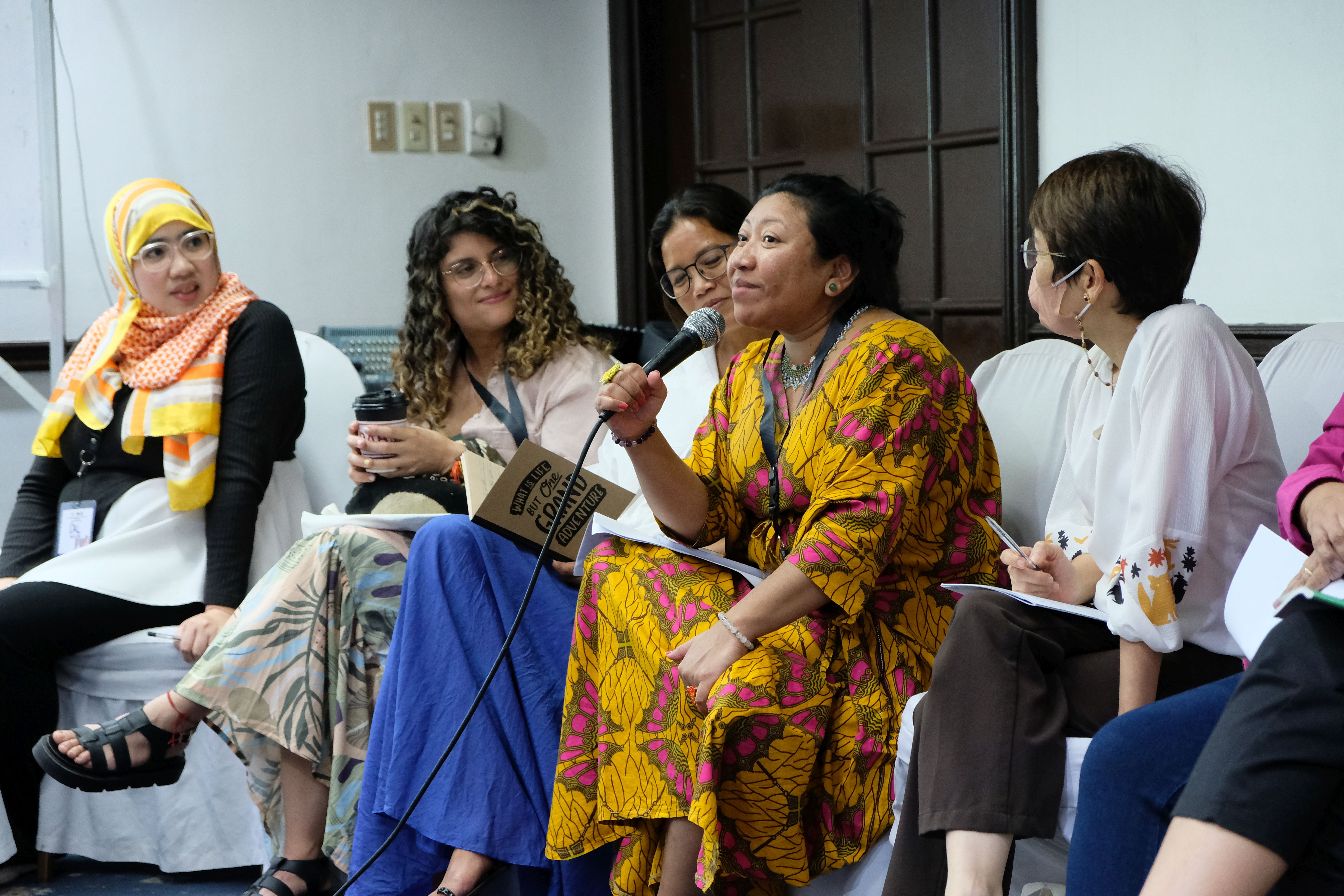 A Colombian woman is speaking into a microphone while women from the Philippines are listening