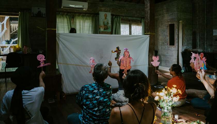 Workshop participant sit behind a white canvas and play a shadow puppet theater with their own individual shadow puppets