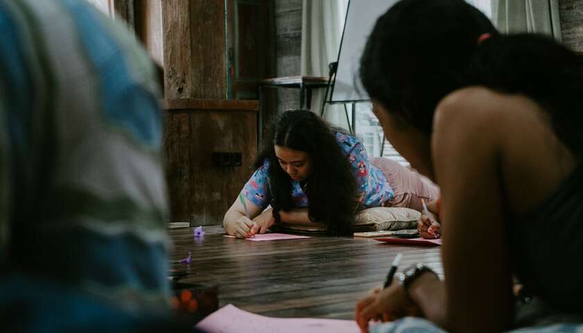 A workshop participant lies on the floor and draws a figure on a pink sheet.