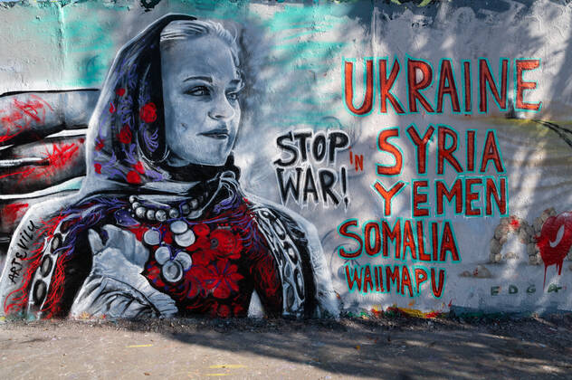 Ein Graffiti auf einer Mauer zeigt eine Frau mit Kopftuch und den Text "Stop War!" sowie die Ländernnamen Ukraine, Syria, Yemen, Somalia und Wallmapu