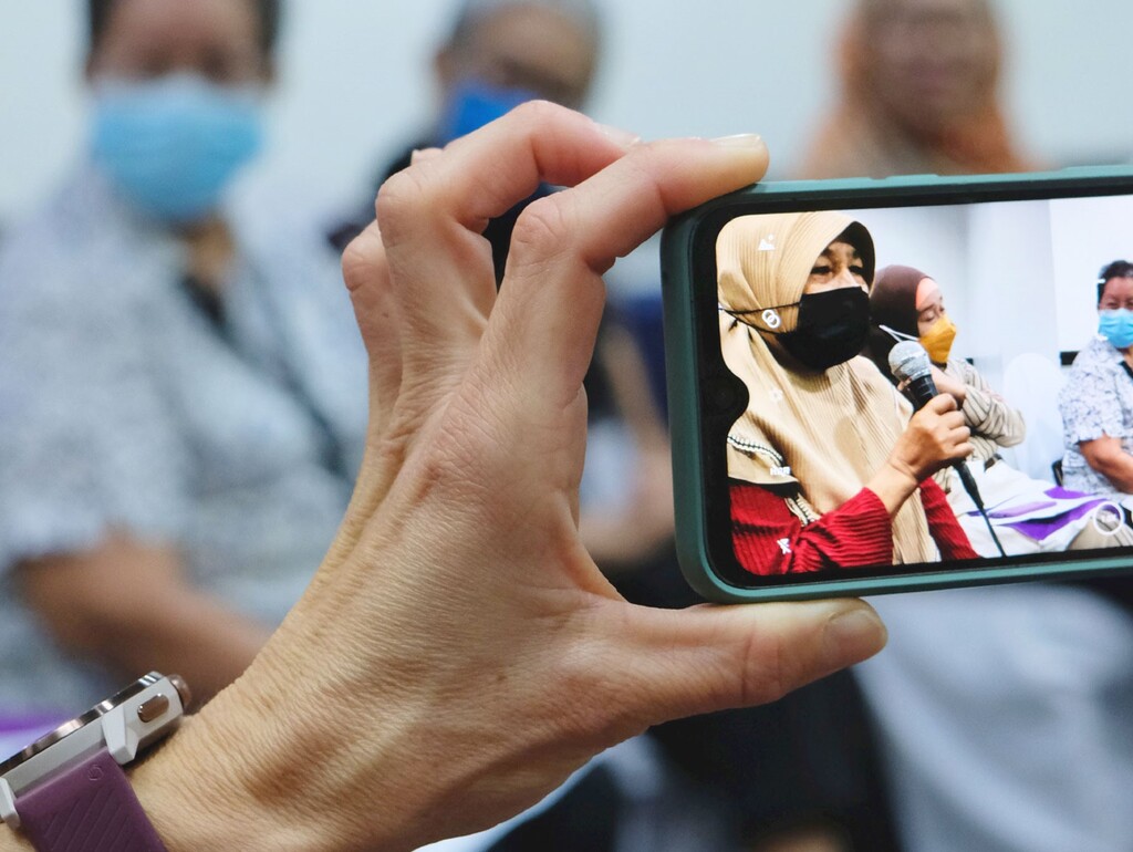 A hand is holding a mobile phone on which a photo of a group of women in the Philippines can be seen.