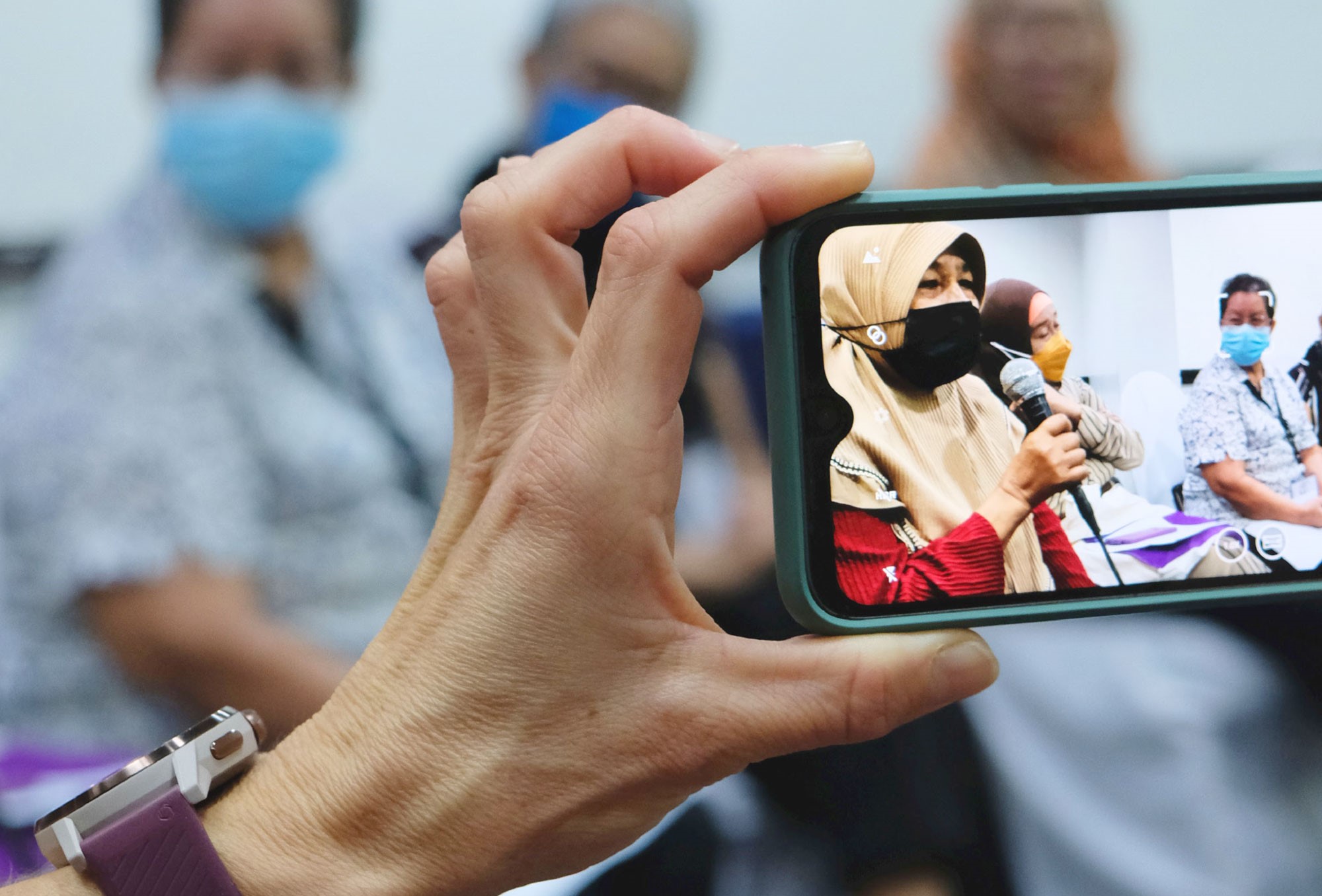 A hand is holding a mobile phone on which a photo of a group of women in the Philippines can be seen.